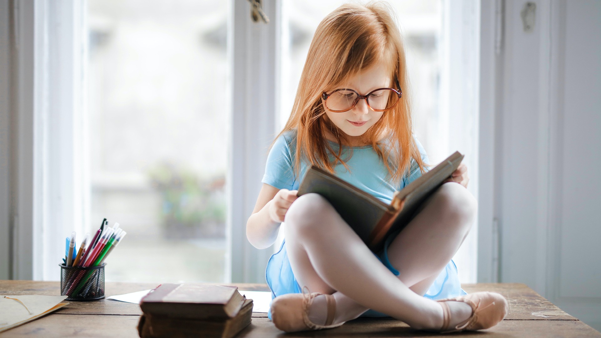 Young girl sitting on desk reading a book about people with disabilities