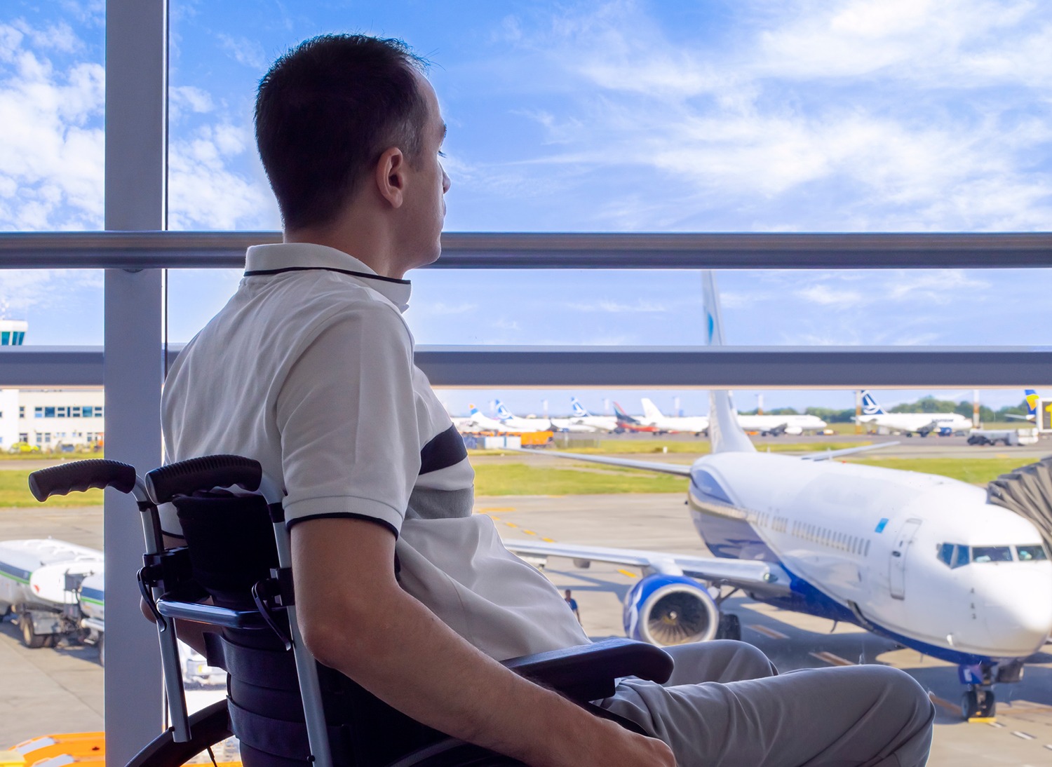 Man using wheelchair sitting in airport looking out the window at a jetliner