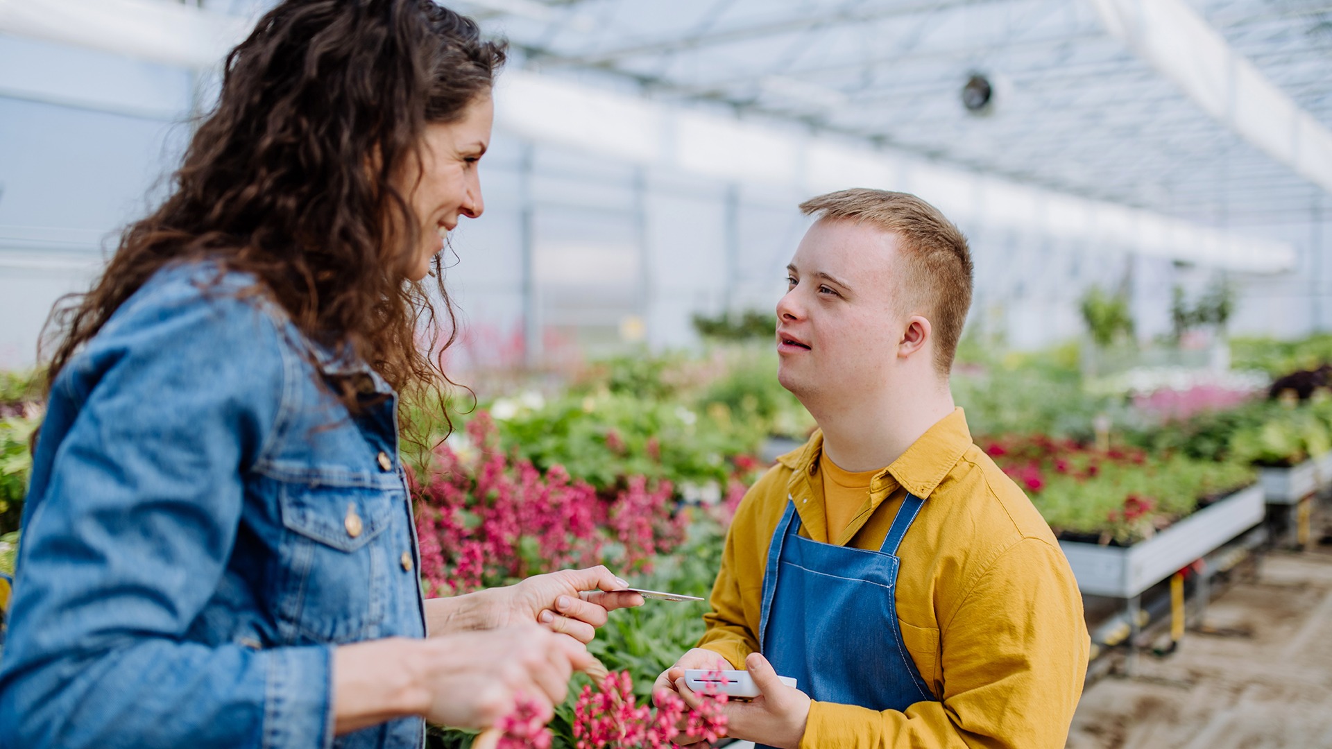 A happy young employee with Down syndrome working in garden centre, taking payment from customer