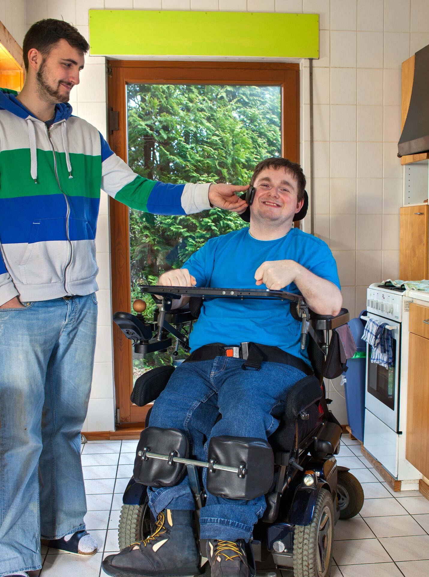 in-home care, male worker standing next holding phone for adult male sitting in wheelchair