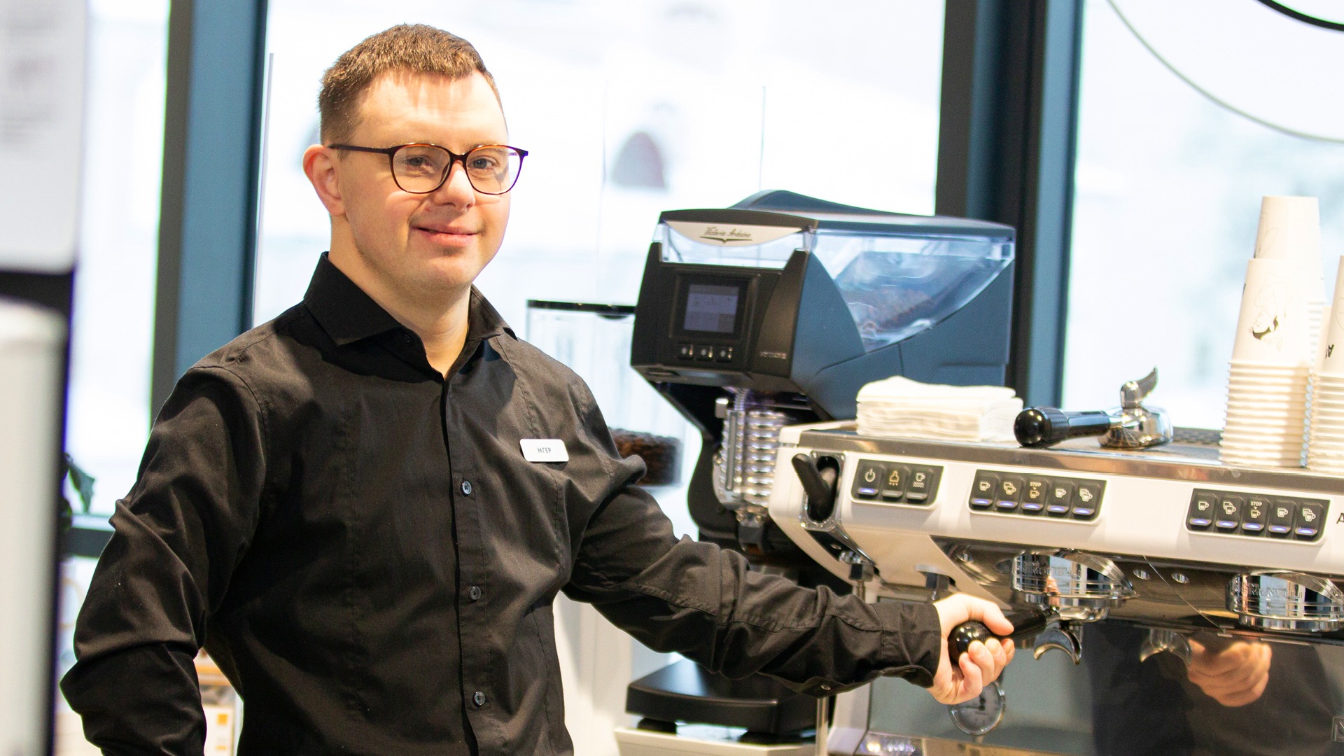 young male barista holding onto handle of espresso machine