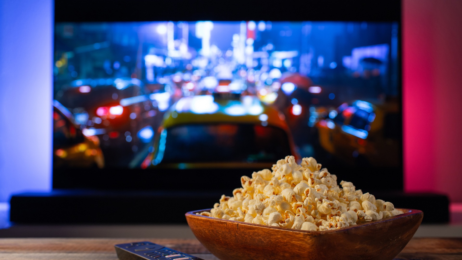 Popcorn and remote control on a table with a TV in the background