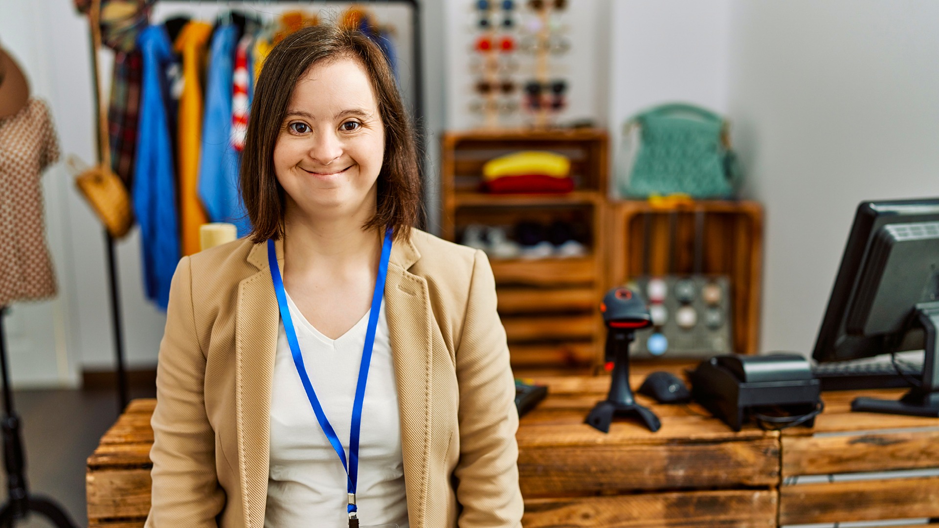 A young woman with down syndrome working as a manager at a retail boutique smiling at camera