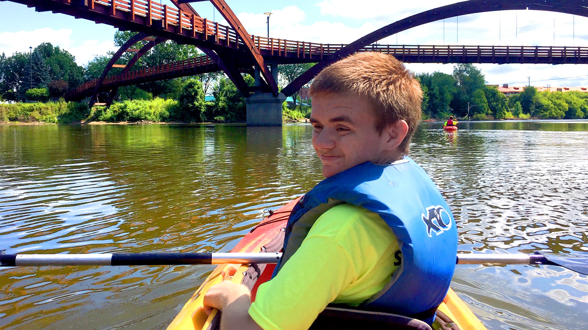 Teenage boy smiling and enjoying kayaking as part of accessible recreation organized by Disability Network Mid-Michigan at an event they held at the Tridge in Midland, Michigan