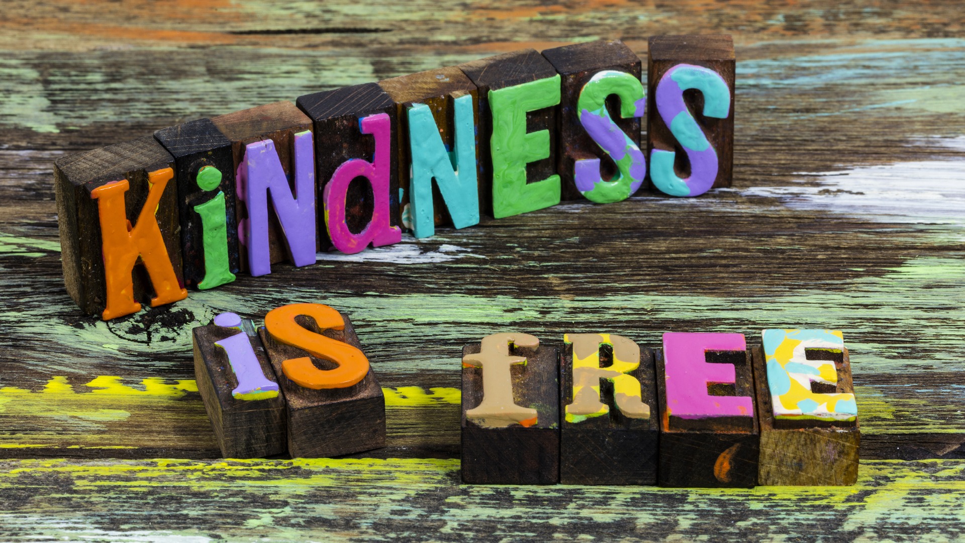 wood block letters painted in multiple bright colors spelling "Kindness is free"