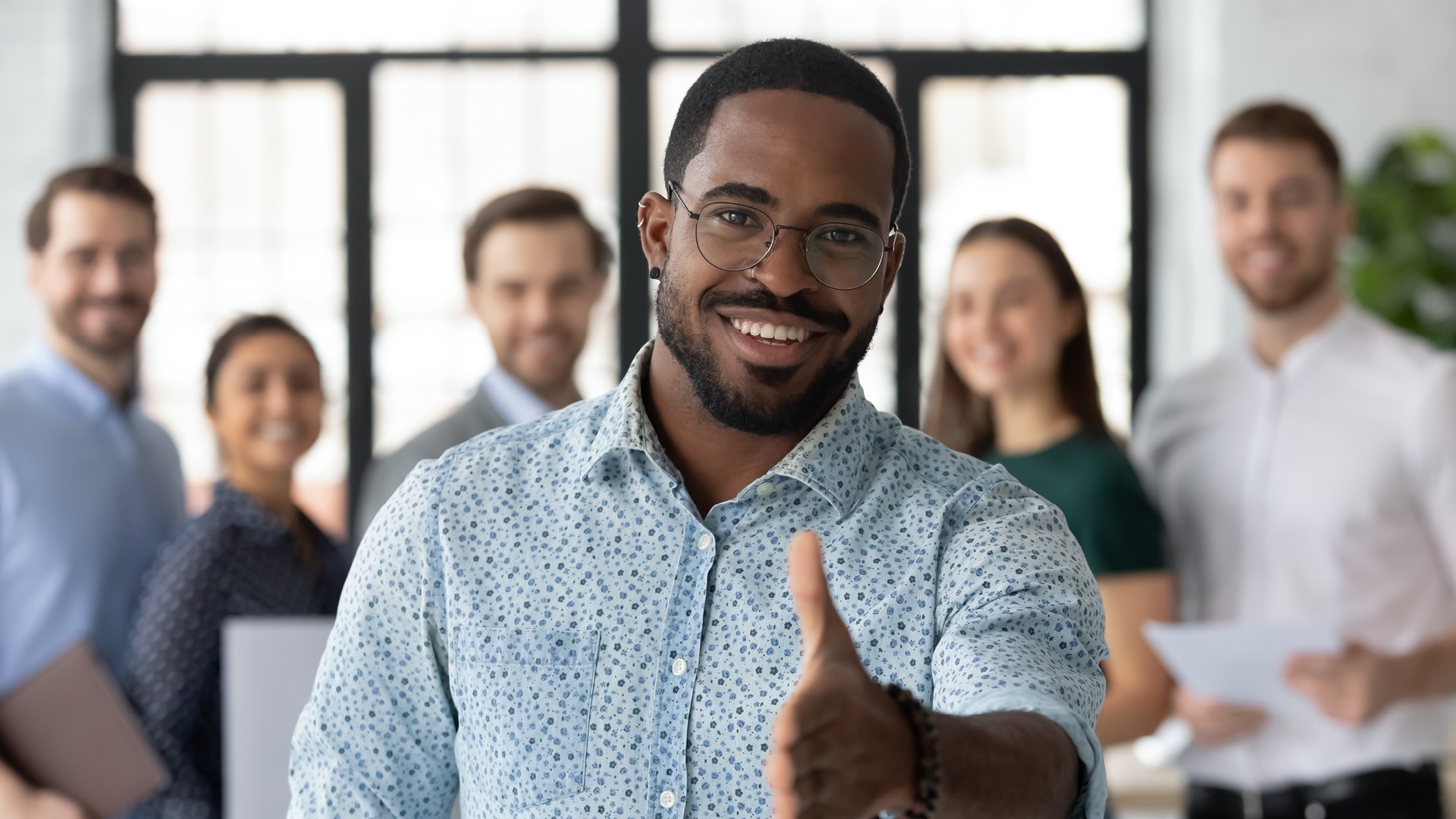 Smiling African American male professional in the office wearing glasses with outstretched hand (ready to shake a hand) welcoming visitors