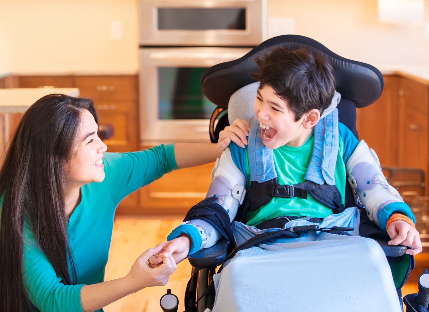 Mom and son with cerebral palsy holding hands and smiling in the kitchen