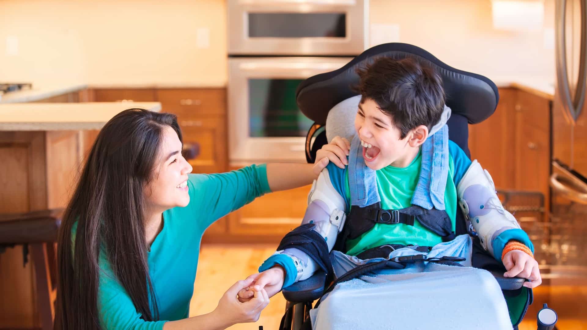 Mom and son with cerebral palsy holding hands and smiling in the kitchen