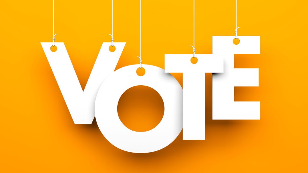 The word vote: white letters on a yellow-orange background. each letter is hanging from white strings.