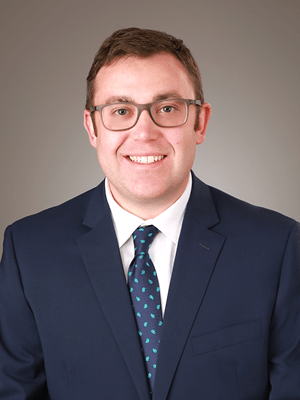 Jacob Kain Portrait smiling wearing glasses and dark suit and tie